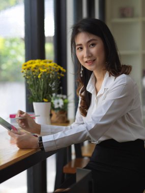 Kafedeki ahşap barda tablet kullanırken kameraya bakan kız öğrencinin portresi