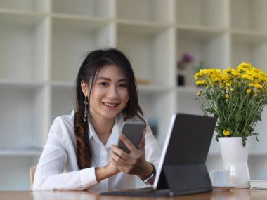 Kafede akıllı telefon ve tabletle çalışırken kameraya bakan kız öğrencinin portresi