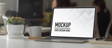 Bilgisayarlı, malzemeli, saksılı ve kahve kupalı çalışma alanının görüntüsü.