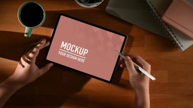 Erkek ellerinin tahta masada dijital tablet kullanışının üst görüntüsü. Not defterleri, kahve fincanları, kesme yolları.
