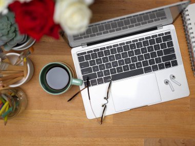 Dizüstü bilgisayarı, bardakları, kahve fincanı ve ahşap masadaki dekorasyonlarla çalışma alanının en üst görüntüsü 