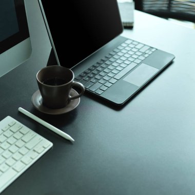 Bilgisayar klavyesi, dizüstü bilgisayarı, kahve fincanı ve kopyalama alanı olan ofis masasının yan görünümü 