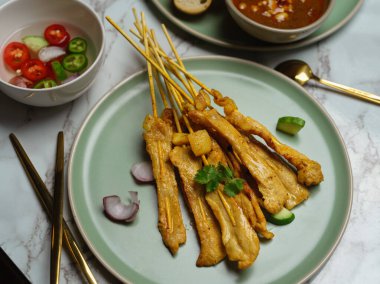 Fıstık sosu ve meze ile servis edilen salatalık ve soğanlı ızgara domuz satay (Moo Satay).