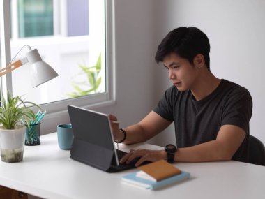 Dijital tablet ve kırtasiyeyle çalışan erkeğin portresi ofis penceresinin yanındaki çalışma masasında. 