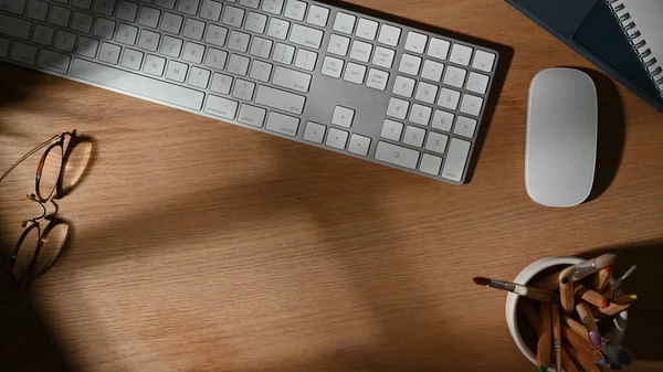 Top view of workspace with computer keyboard, supplies and copy space on wooden table