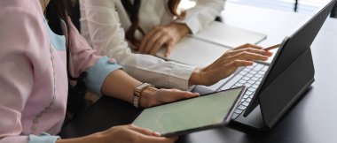 Toplantı odasında dizüstü bilgisayar ve tabletle çalışan iki kadın çalışanın yan görüntüsü