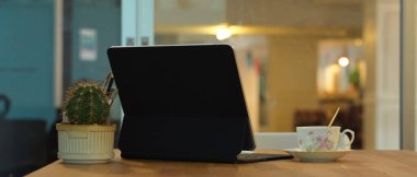 Tablet, kahve fincanı ve kaktüs tenceresini ofis odasındaki ahşap masada kapat.