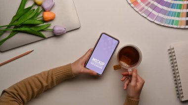 Akıllı telefon kullanan ve çalışma alanında kahve fincanı tutan kadınların üst görünümü, kırpmayı içerir 