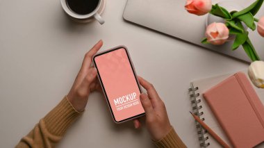 Kadınsı çalışma alanında akıllı telefonu tutan kadınların üst görünümü, kırpma yolunu da içerir