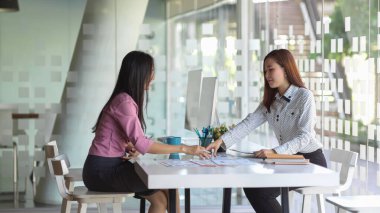 Ofis odasındaki ofis malzemeleriyle projelerine danışmanlık yapan iki iş kadınının yan görünüşü