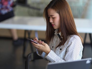 Ofiste dinlenirken akıllı telefon kullanan iş kadınının yan görüntüsü