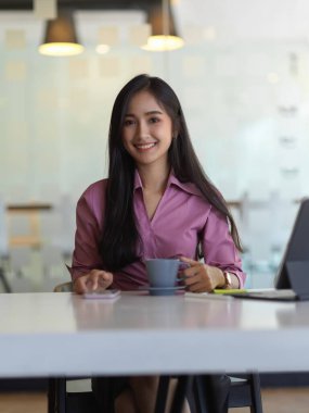 İş kadınının portresi. Akıllı telefon kullanıyor ve çalışma odasında kahve fincanı tutuyor.