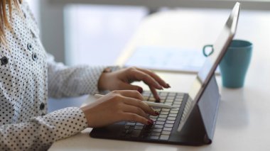 Tablet klavyesinde kahve fincanıyla çalışan kadınların yan görünümü
