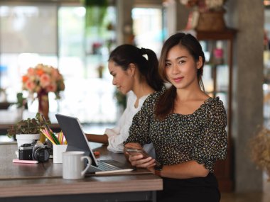 İş arkadaşıyla toplantı odasında buluşurken kameraya gülümseyen bir iş kadını portresi.