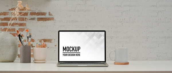 Close up view of workspace with laptop, supplies, paint brushes and decoration in home office