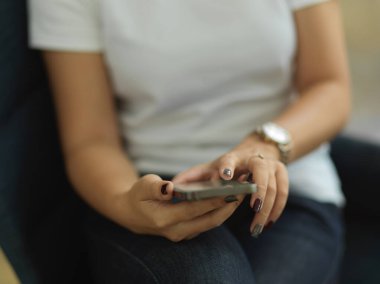 Kol sandalyesinde rahatça otururken akıllı telefon kullanan bir kadının görüntüsünü kapat 