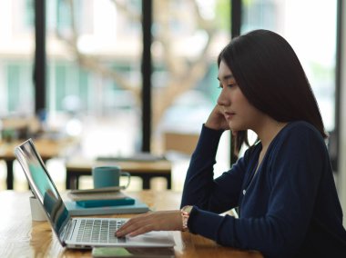 Kütüphanede dizüstü bilgisayarla ödev yapan bayan üniversite öğrencisinin yan görüntüsü