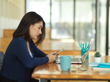 Birlikte çalışma alanında ödev yaparken akıllı telefon kullanan kız üniversite öğrencisinin yan görünümü