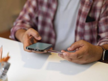 Ofis odasındaki beyaz masada akıllı telefon kullanan bir iş adamı görüntüsü.