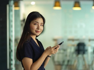 Ofiste akıllı telefon kullanırken kameraya gülümseyen iş kadınının yan görüntüsü