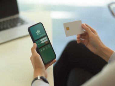 Çevrimiçi akıllı telefondan ödeme yaparken kredi kartı tutan iş kadınının görüntüsünü kapat