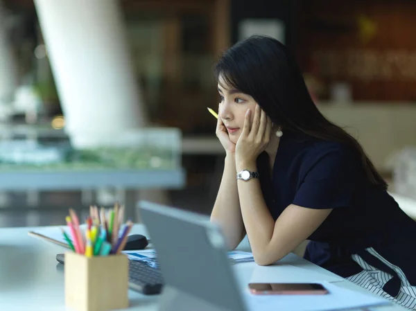 Side view of female office worker thinking about her project while working with office supplies in office