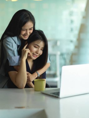 Modern oturma odasında dizüstü bilgisayarla sarılan genç kız kardeşlerin kırpılmış görüntüleri. 