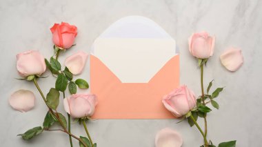 Makyaj kartının üst görüntüsü, pastel zarf ve mermer masadaki pembe güller.