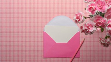 Masada pembe Scott masası, kart, pembe zarf, kalem ve pembe çiçek var.