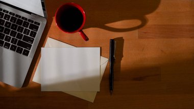 Çalışma alanının üst görüntüsü. Çalışma odasında kart, kalem, dizüstü bilgisayar ve kahve kupası var.