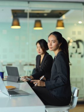 Ofis odasında iş arkadaşıyla çalışırken kameraya bakan genç iş adamlarının yan görüntüsü