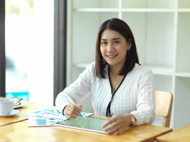 İşkadını portresi tablet ve kağıt işleriyle ahşap masa üzerinde çalışıyor.