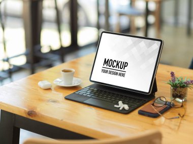 Dijital tabletin yan görünümü arasında kırpma yolu, aksesuarlar ve ahşap masadaki kahve fincanı yer alıyor