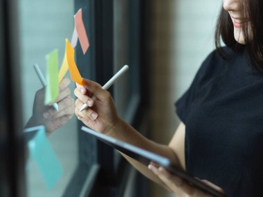 Dijital tabletle çalışan kadınların yakın görüntüsü ve ofisteki cam duvardaki yapışkan nota dair bir fikir almak