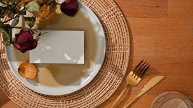 Tabakta sahte isim kartı, çatal, masa bıçağı ve çiçekle süslenmiş yemek takımının en üst görüntüsü.
