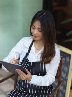 Kafesinde kahve masasında otururken dijital tablet kullanan bayan baristanın en iyi görüntüsü.