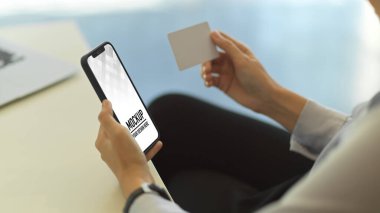 Ofiste çalışırken elinde akıllı telefon ve isim kartı olan bir kadının yan görüntüsü.