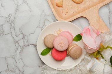 Üzerinde güllerle süslenmiş bir tabak Fransız rengarenk badem kurabiyesi olan mermer yemek tablası manzarası.