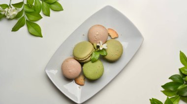 Beyaz masa, yapraklarla süslenmiş bir tabak renkli badem kurabiyesi.