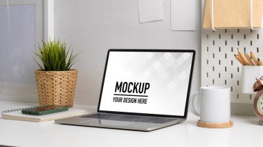 Bilgisayarlı, kırtasiyeli, bardaklı ve saksılı çalışma alanının görüntüsü.