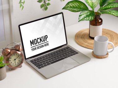 Laptop, bardak, dekorasyon ve bitki vazosuyla çalışma alanının görüntüsü.