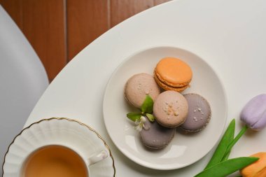 Fransız rengarenk badem kurabiyeleri, çay fincanı ve lalelerin oturma odasındaki sehpanın üzerindeki manzarası.