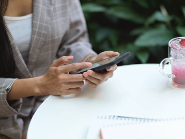 Bahçe bahçesinde dinlenirken akıllı telefon kullanan kadın elinin kırpılmış görüntüsü. 