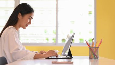 Çalışma alanında klavye dizüstü bilgisayarında yazarken projesinde çalışan genç ve güzel tasarımcının yan görünümü