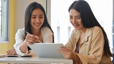 Kütüphanede dijital tabletle ödev yapan iki güzel kız öğrencinin portresi.