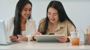 Dijital tablet üzerinde grup ödevi yaparken iki kız öğrencinin birbirini kucaklamasını yakından izle