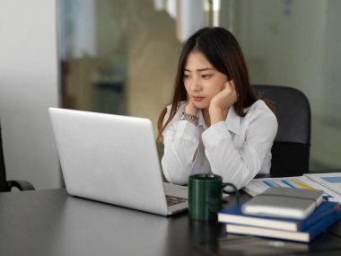 Ofis odasında dizüstü bilgisayarla işine konsantre olan kadın ofis çalışanının portresi.