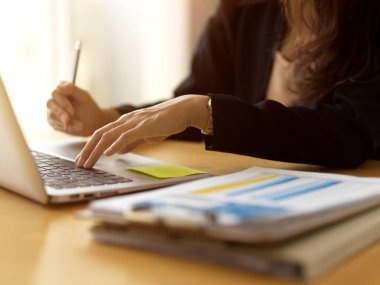 İş kadınının laptopla ve ahşap masadaki evrak işleriyle çalışmasını yakından izleyin.