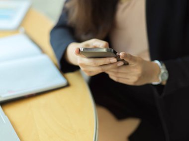 İş yerinde evrak işleriyle uğraşırken akıllı telefon kullanan bir iş kadınının görüntüsünü kapat 