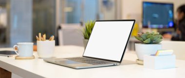 Ofis odasındaki masanın üzerine dizüstü bilgisayar kırtasiyesi, fincan ve saksı ile taşınabilir çalışma alanının kırpılmış görüntüsü.